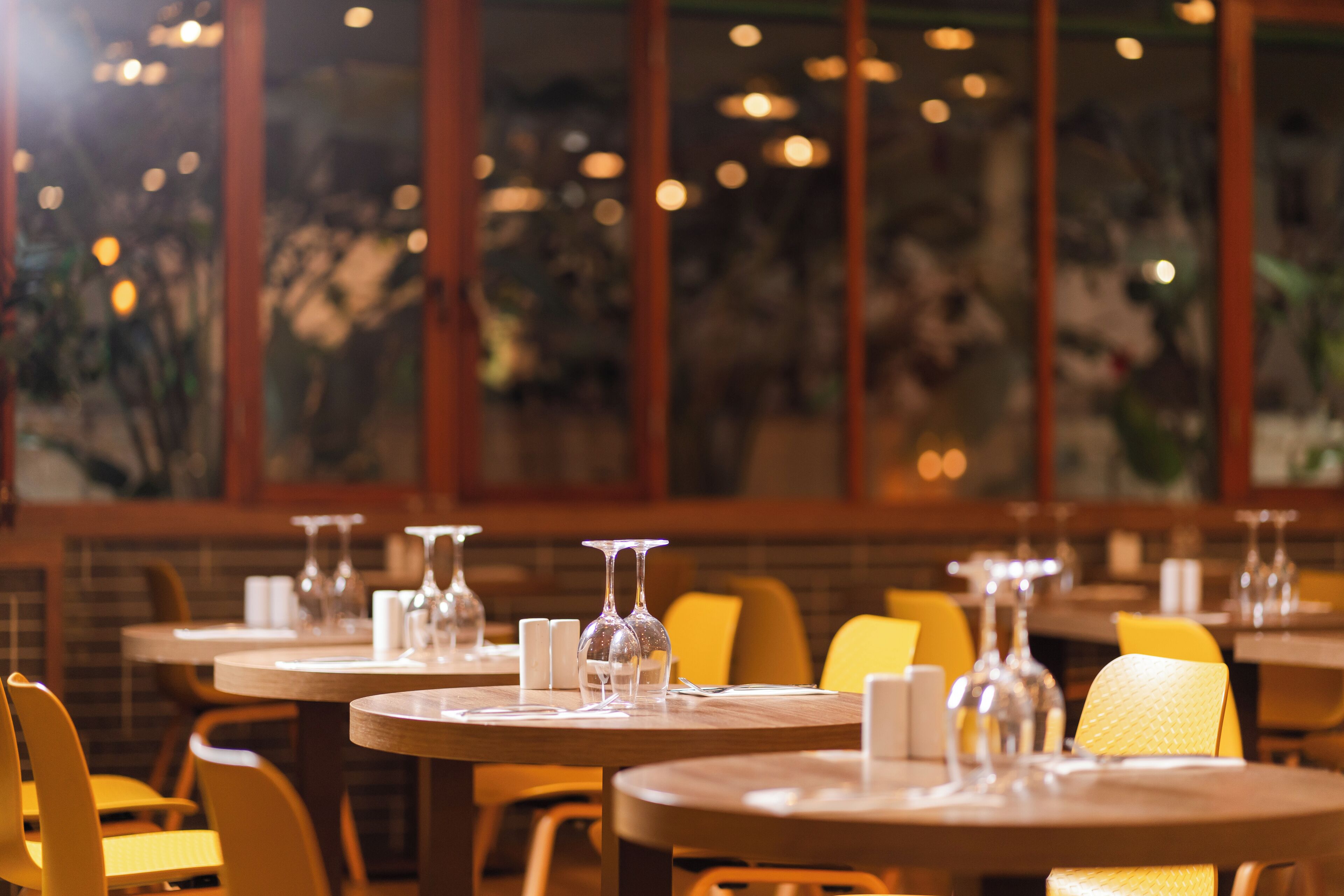 Un restaurante con mesas redondas, sillas amarillas y cristalería en cada mesa.