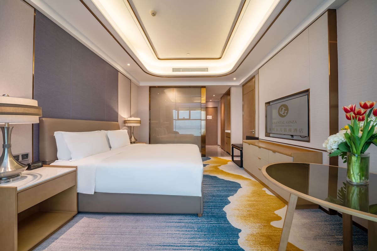 A hotel room with a large bed, a desk, a chair, a TV, and a vase with flowers.