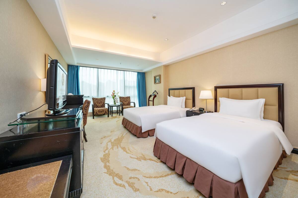 A hotel room with two beds, a desk, a television, and a seating area with chairs and a table.