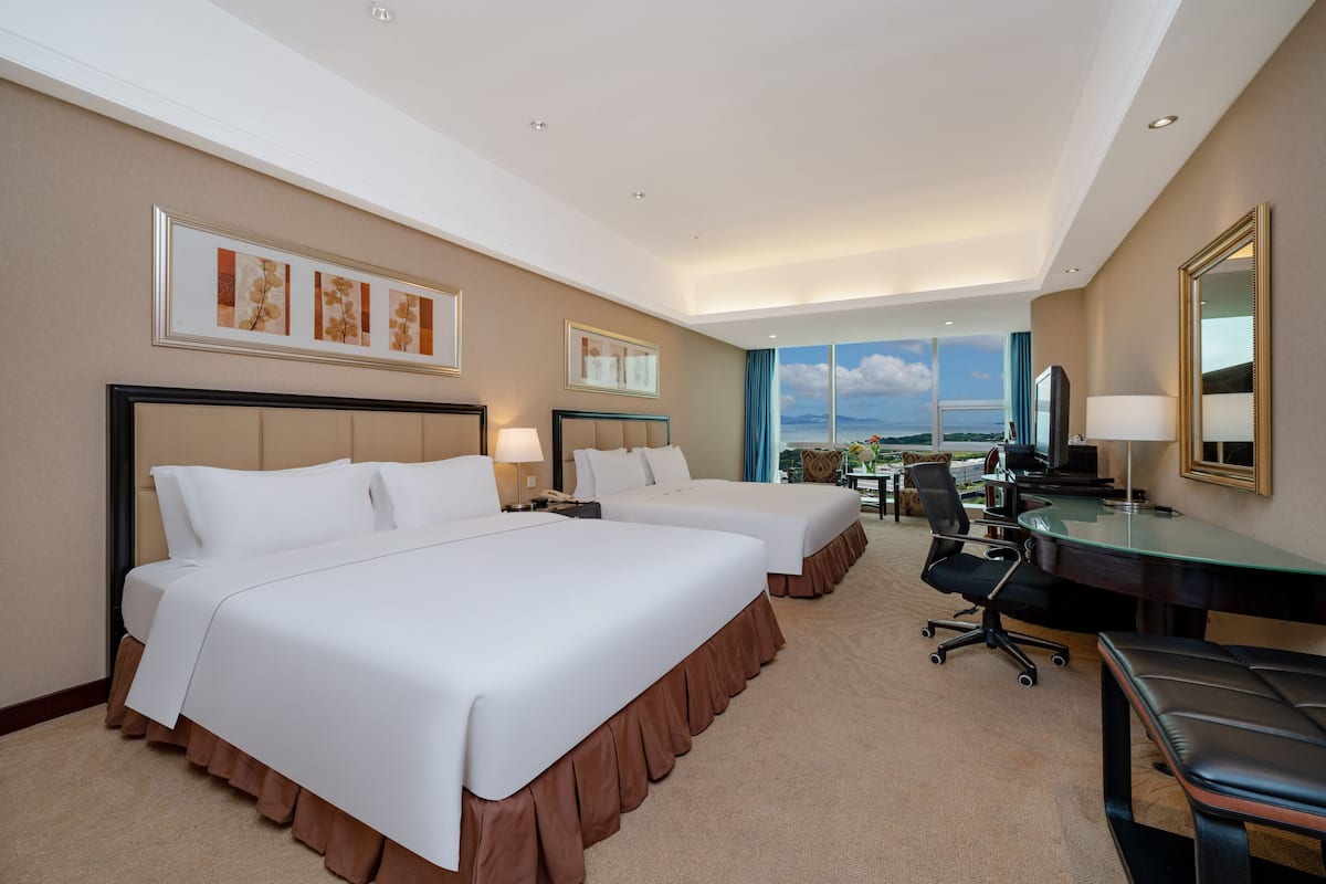 A hotel room with two beds, a desk, a chair, and a large window with a view.