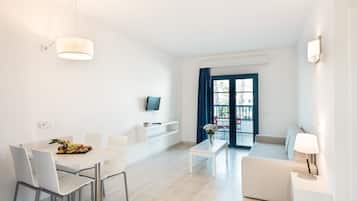 A modern living room with a sofa, a dining table with chairs, a TV mounted on the wall, and a window with curtains.