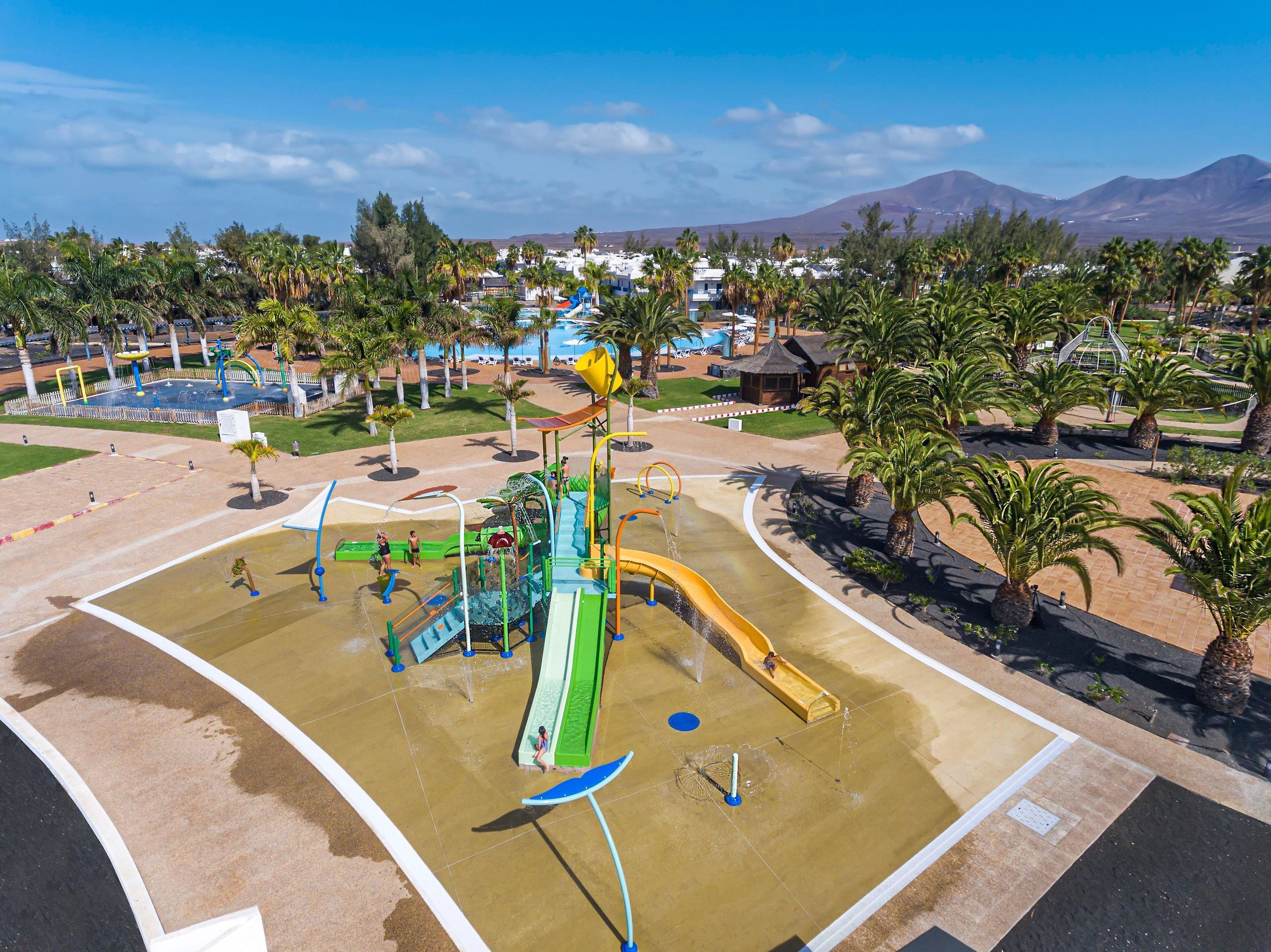 Ein Wasserpark mit Rutschen und Spielgeräten, umgeben von Palmen und einem Pool.