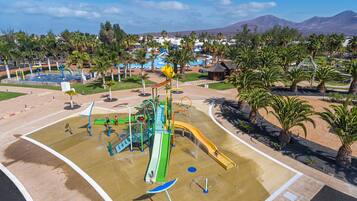 Ein Wasserpark mit Rutschen und Spielgeräten, umgeben von Palmen und einem Pool.