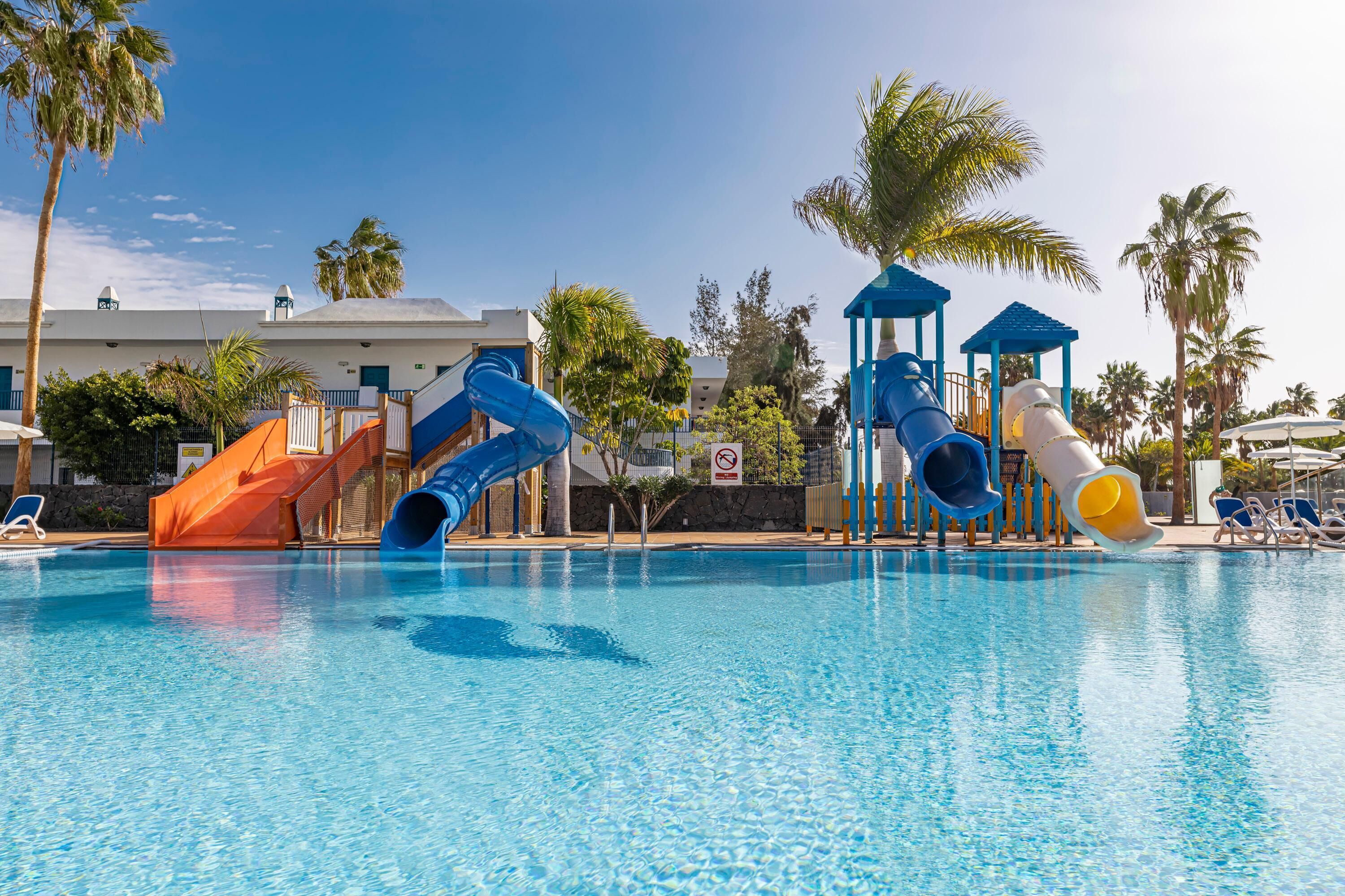 Ein Pool mit mehreren Wasserrutschen, Palmen und Liegestühlen.