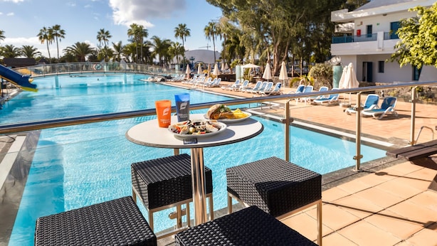 A poolside area with lounge chairs, a table with food, and a pool. - THB Tropical Island Aparthotel (Yaiza)