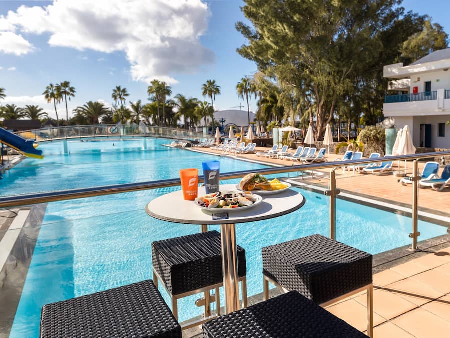 A poolside area with lounge chairs, a table with food, and a pool.
