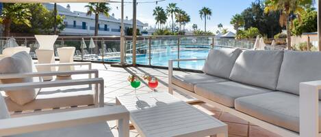 A poolside area with a white sofa, lounge chairs, and a small table.