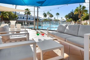 Een zwembadgedeelte met een witte bank, loungestoelen en een bijzettafeltje.