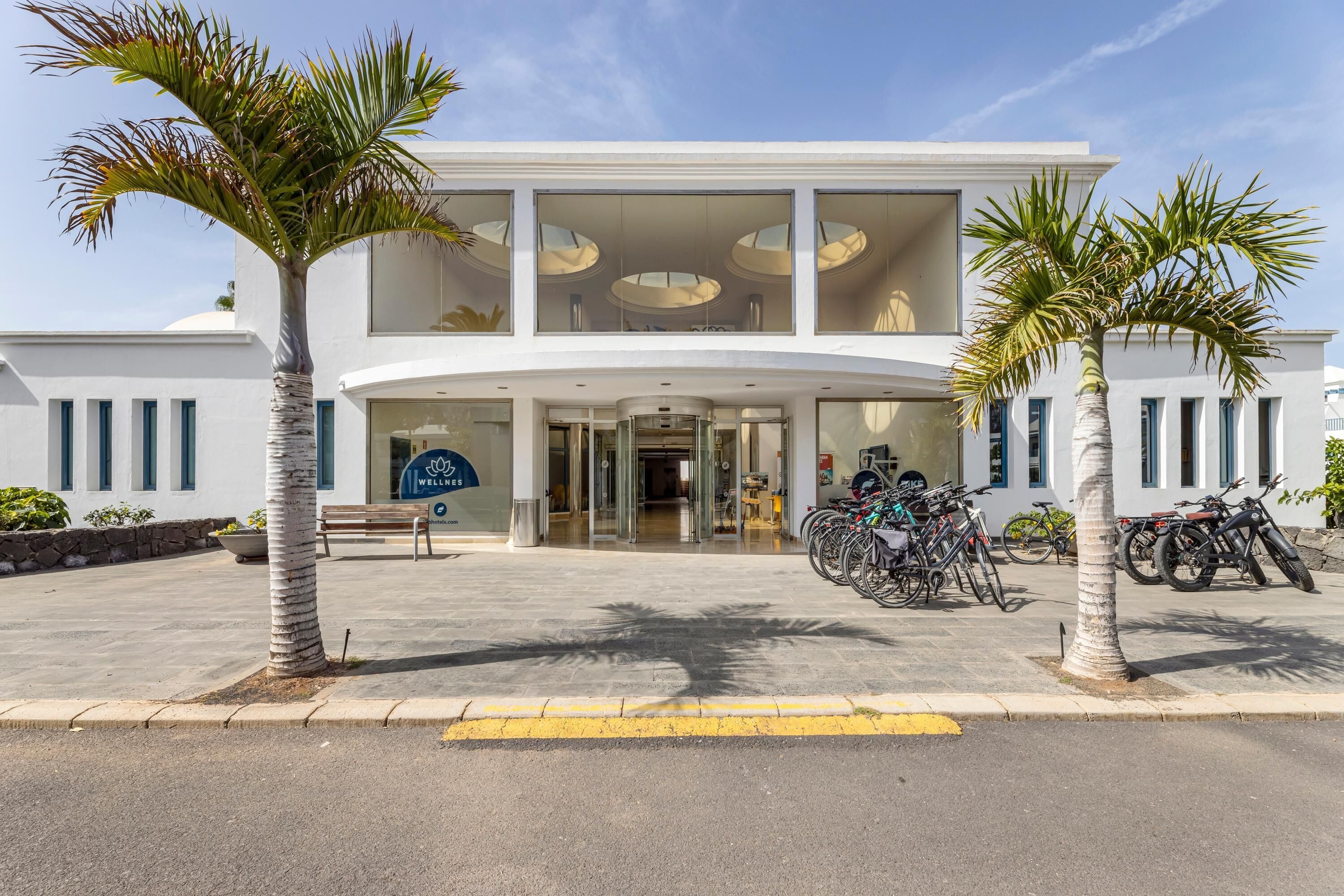 Un hotel moderno con una entrada curva, un espacio para bicicletas y palmeras.