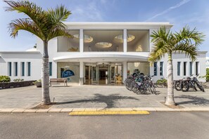 A modern hotel with a curved entrance, a bike parking area, and palm trees. - THB Tropical Island Aparthotel (Yaiza)