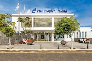 The exterior of THB Tropical Island hotel with a clear entrance, outdoor seating, and flags. - THB Tropical Island Aparthotel (Yaiza)