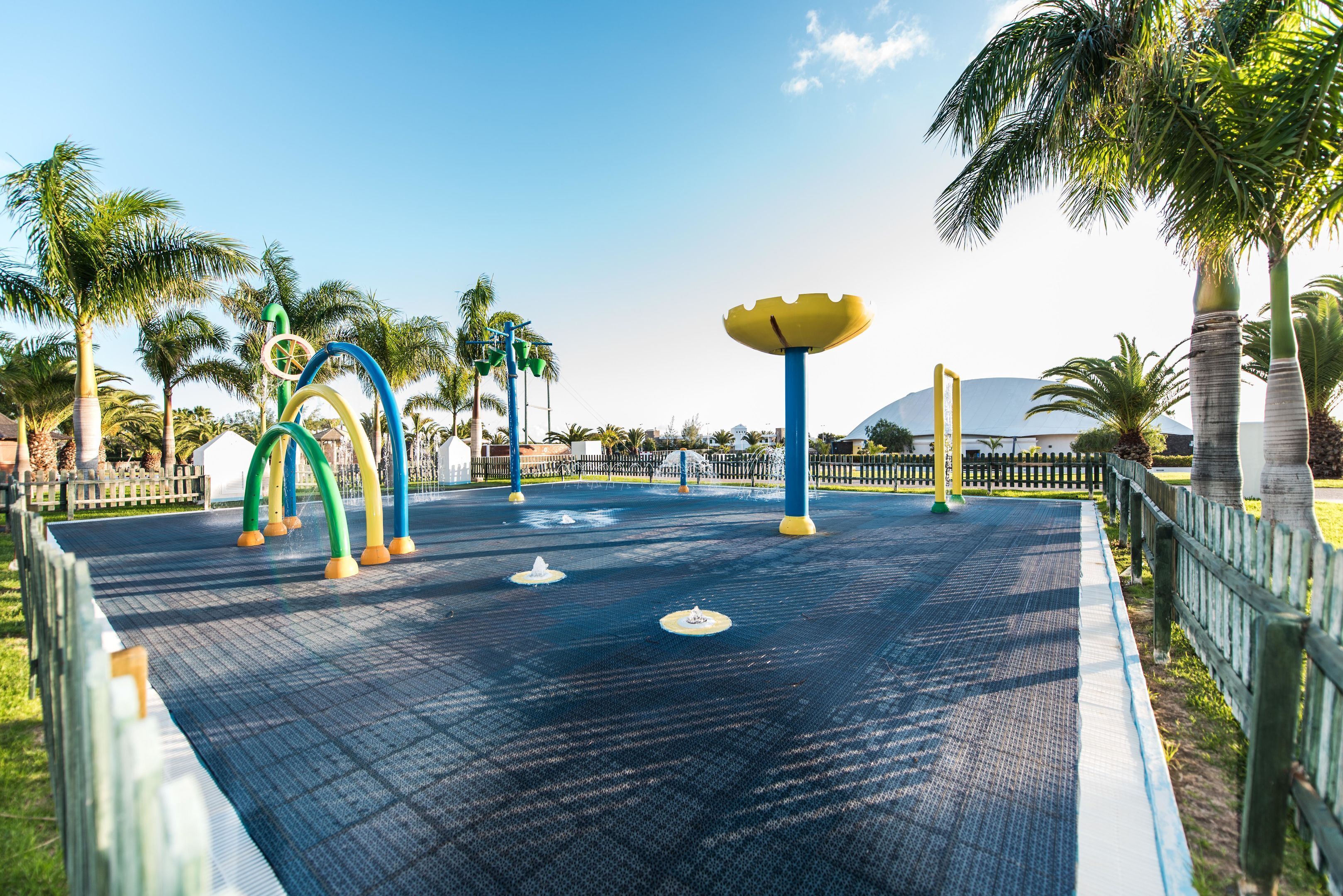 A playground with colorful play structures and palm trees.