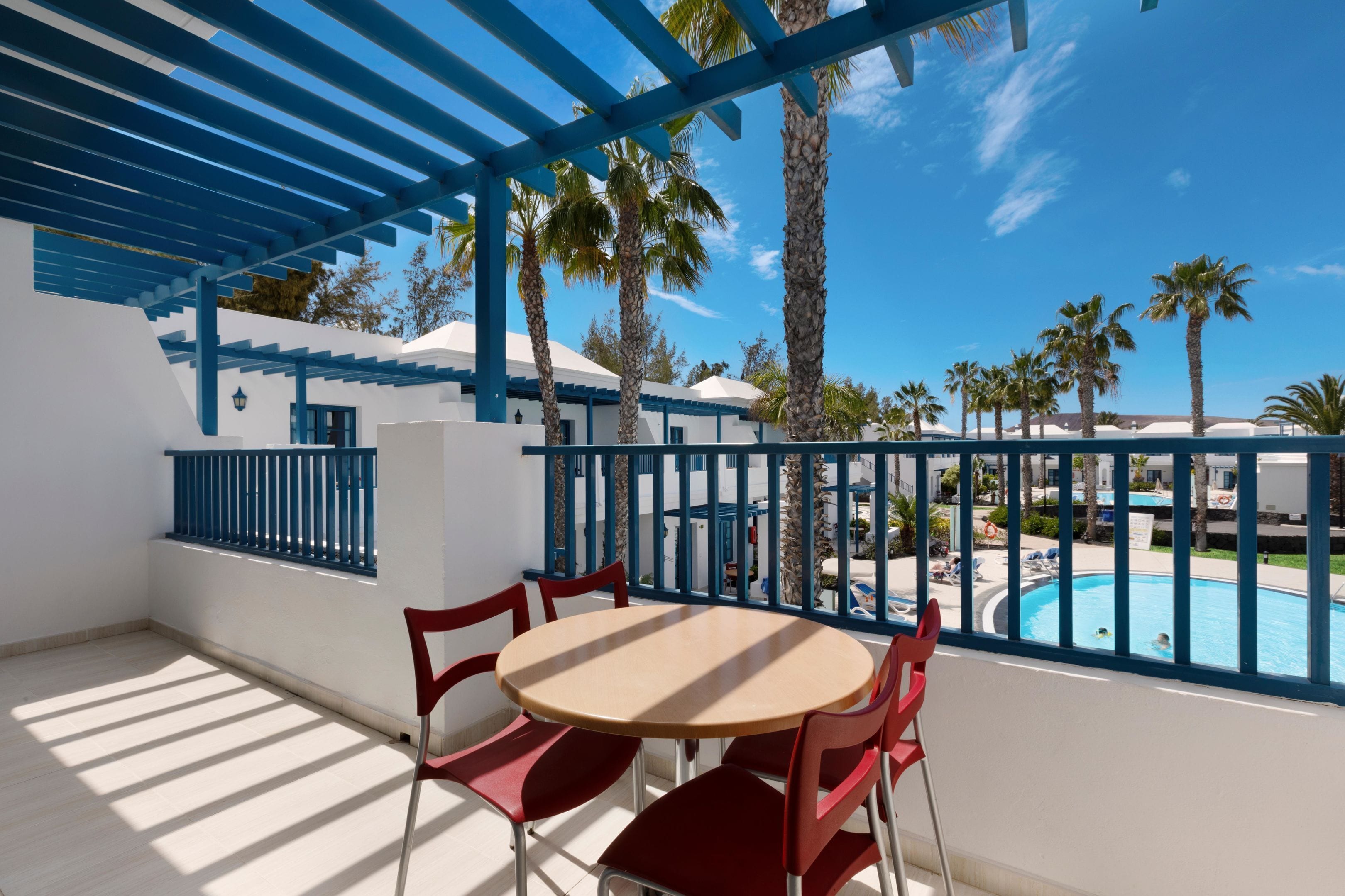 A terrace with a pool view, red chairs, and a blue pergola.