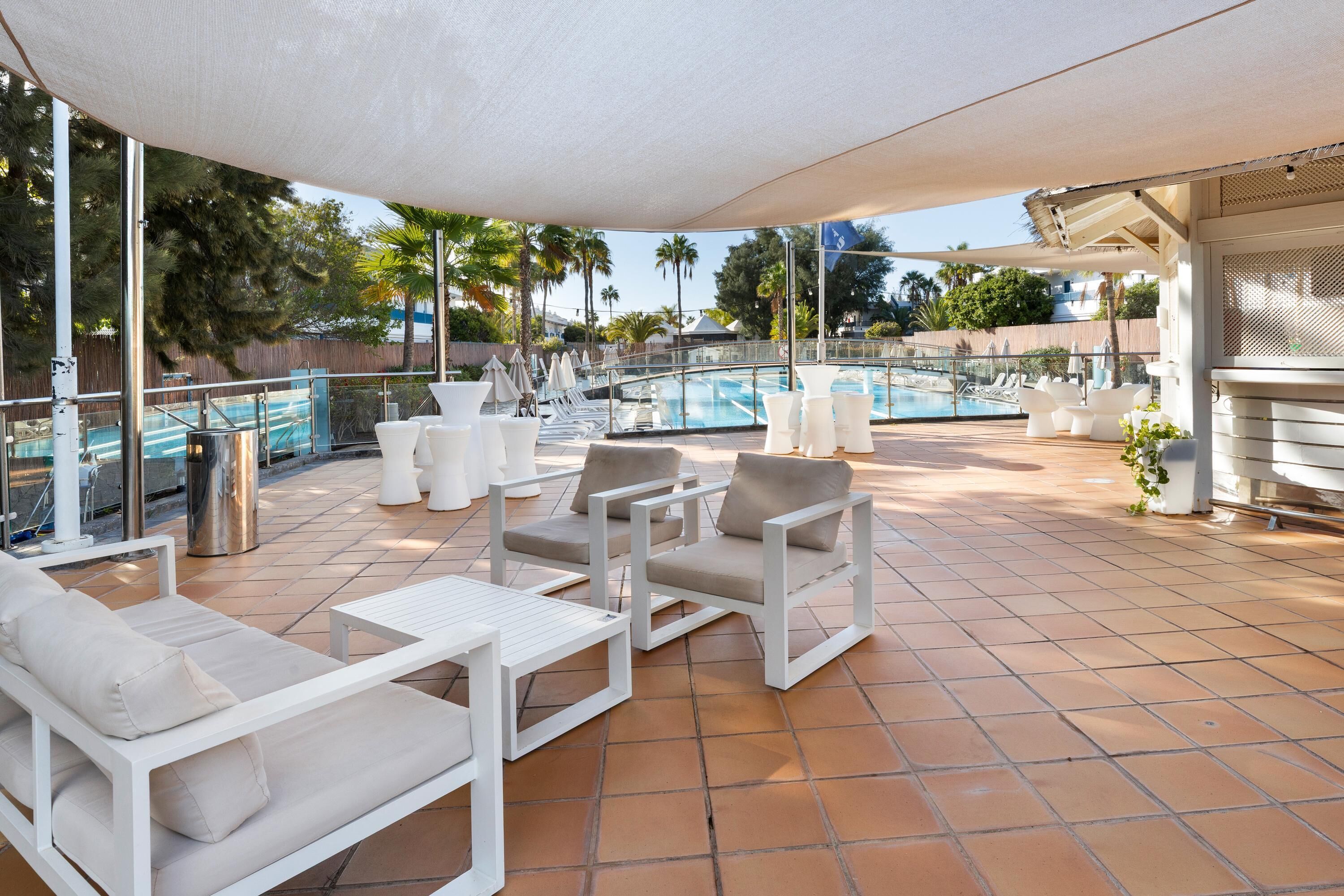 A rooftop pool area with white outdoor furniture, including sofas and chairs, and a covered seating area.