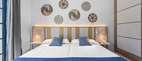 A double bed with a blue blanket, two pillows, a bedside table with a lamp, and wall decor.