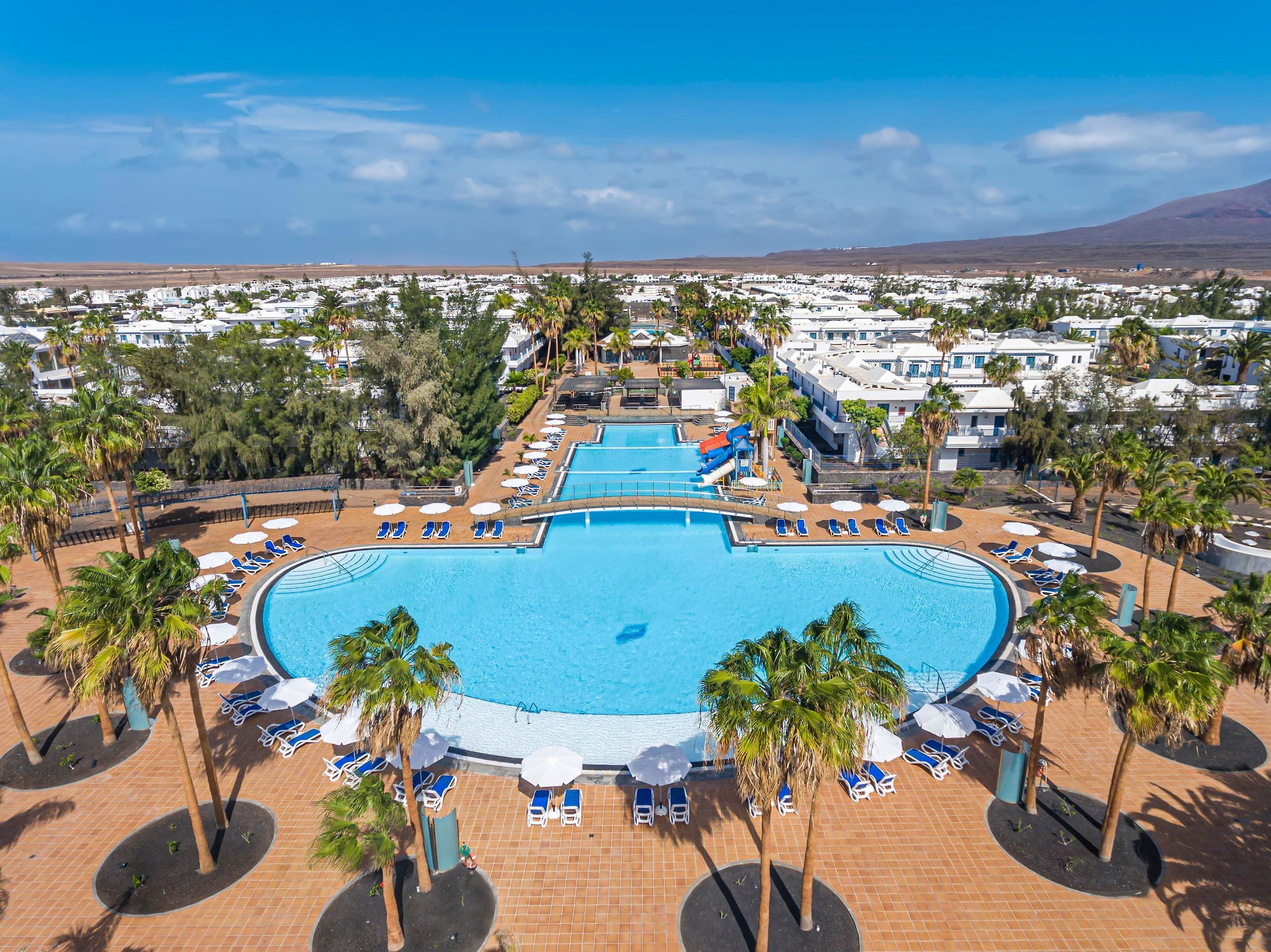 Un complex turístic amb diverses piscines, palmeres i zones de relaxació.