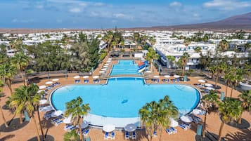 Un complejo turístico con varias piscinas, palmeras y zonas de descanso.