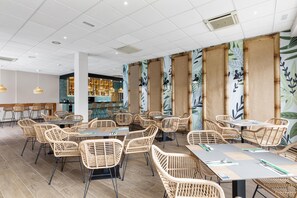 Ein geräumiger Innenbereich mit Essbereich, ausgestattet mit Korbtischen und -stühlen, eine Bar mit Flaschenregalen und eine Decke mit eingelassener Beleuchtung.