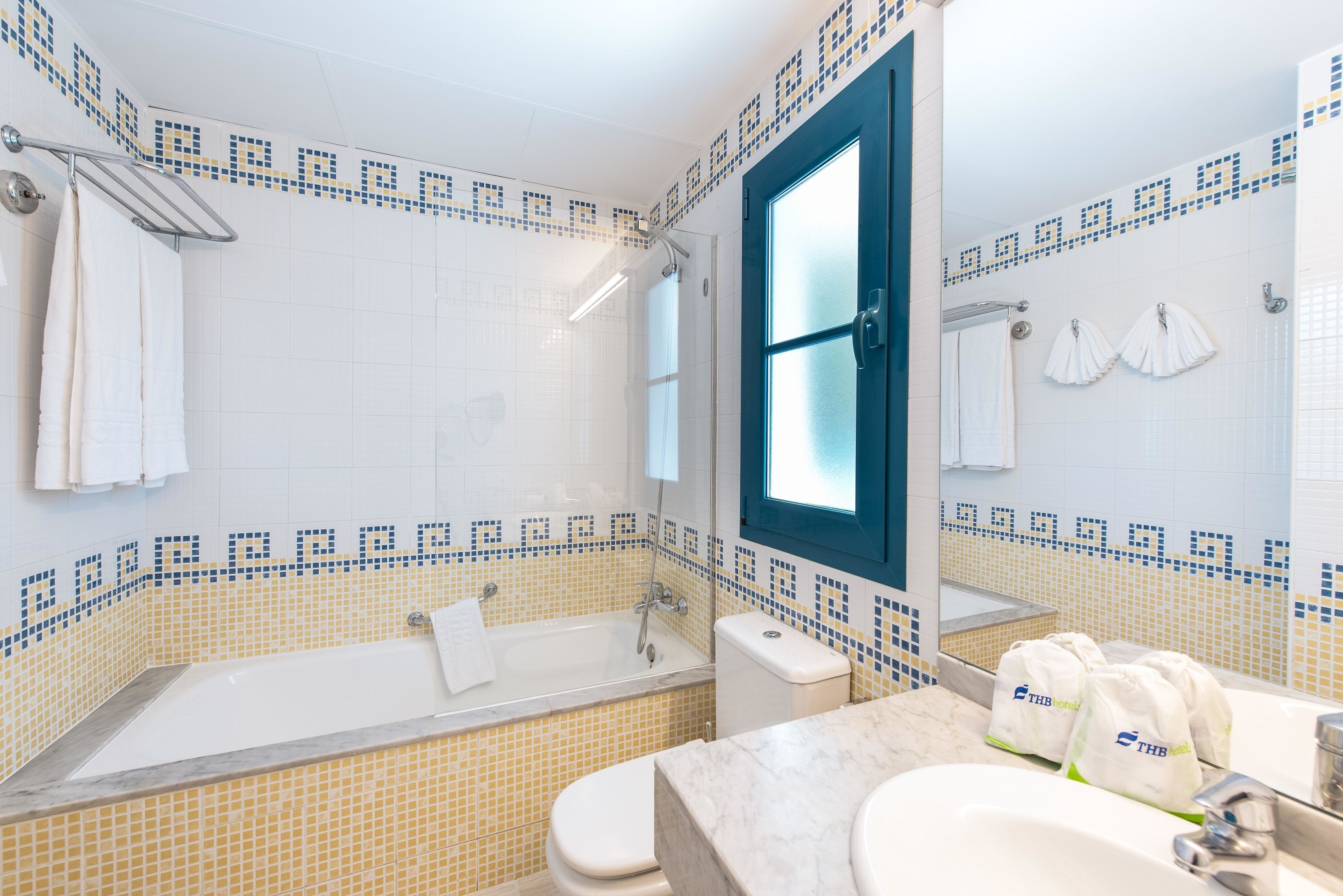 Une salle de bain équipée d’une baignoire, de toilettes et d’un lavabo, avec un mur recouvert de carreaux et une fenêtre.