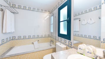 Une salle de bain équipée d’une baignoire, de toilettes et d’un lavabo, avec un mur recouvert de carreaux et une fenêtre.