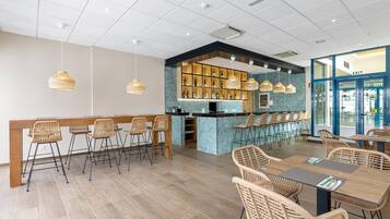 A modern restaurant with a bar area, wooden flooring, and wicker chairs.