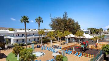 Un resort con zona de piscina, tumbonas, palmeras y parque infantil.