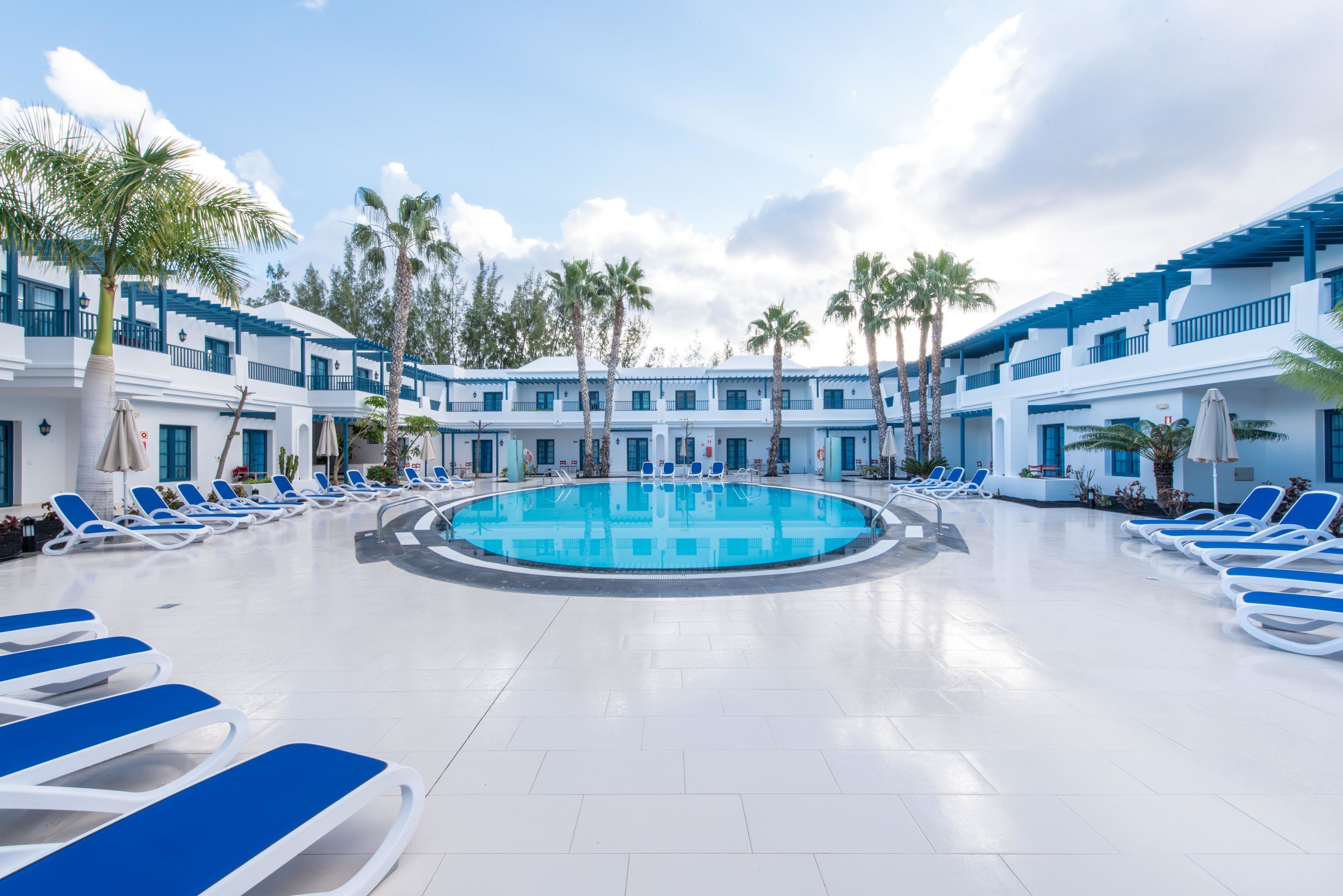 A pool area with blue and white lounge chairs, a central pool, and palm trees.
