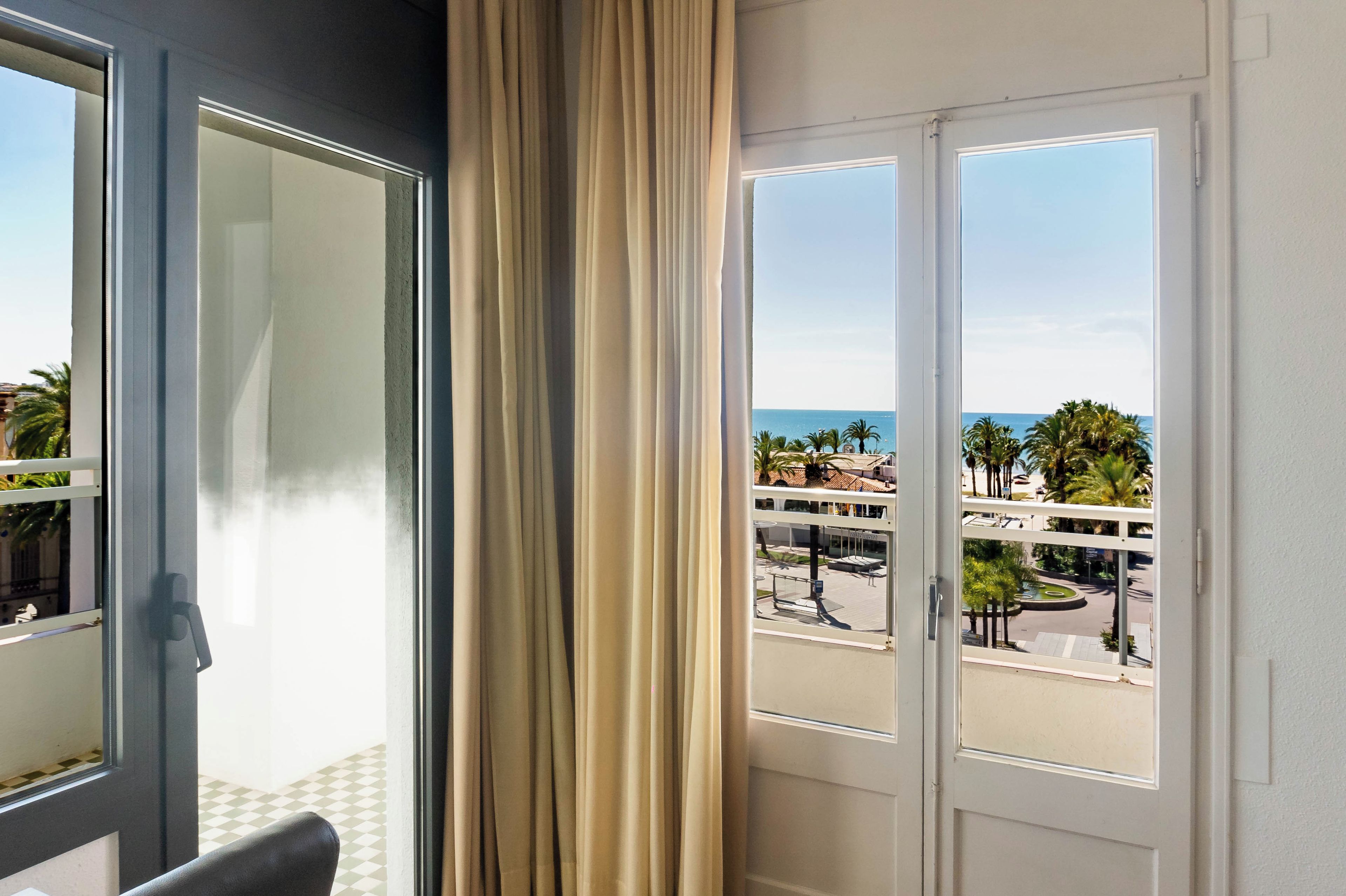 A room with a view of a coastal area, including palm trees and a road.