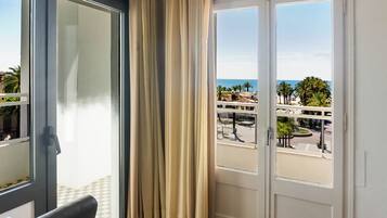 A room with a view of a coastal area, including palm trees and a road.