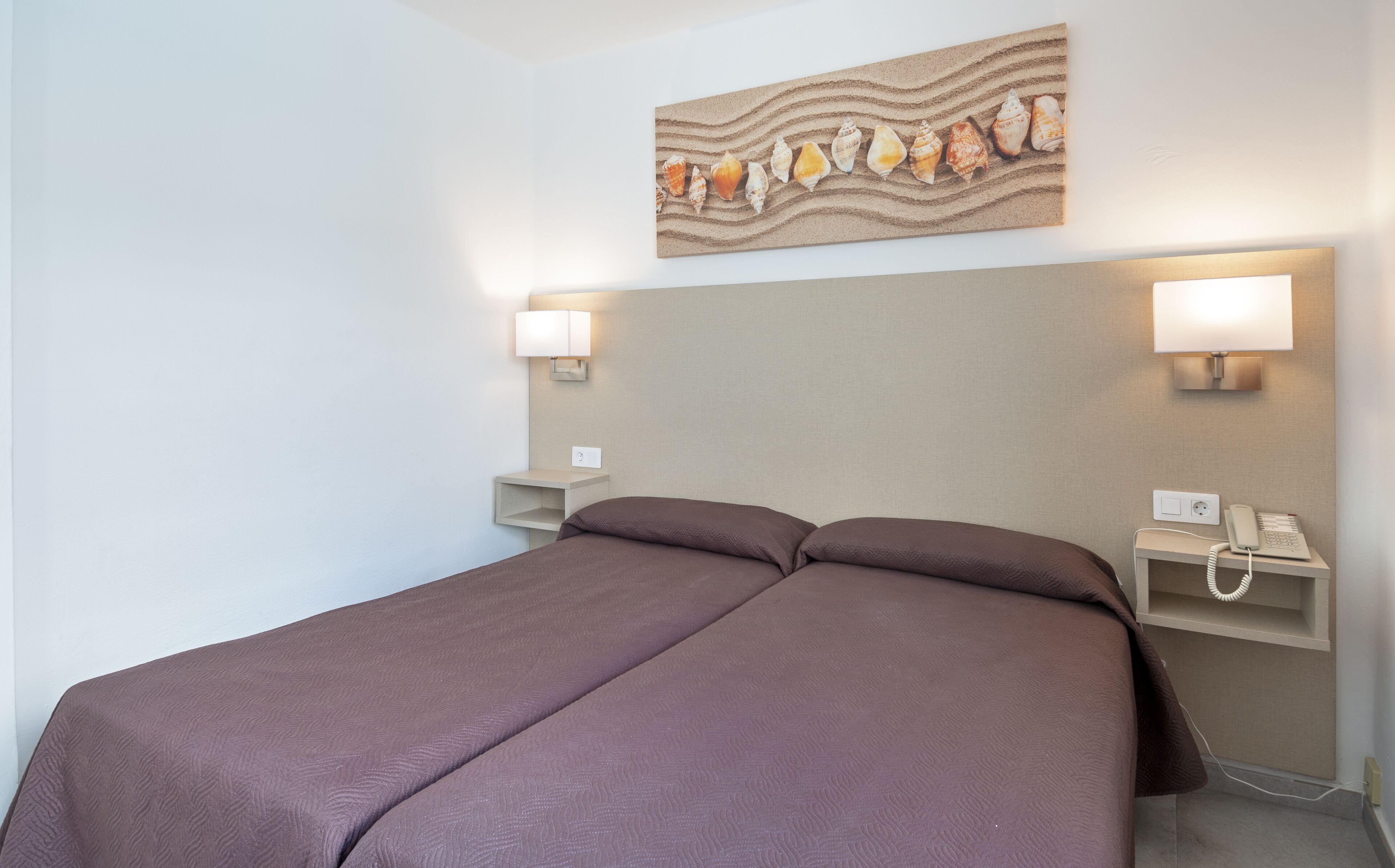 Una camera d'albergo con un letto, due comodini, un telefono e un'opera d'arte appesa al muro.