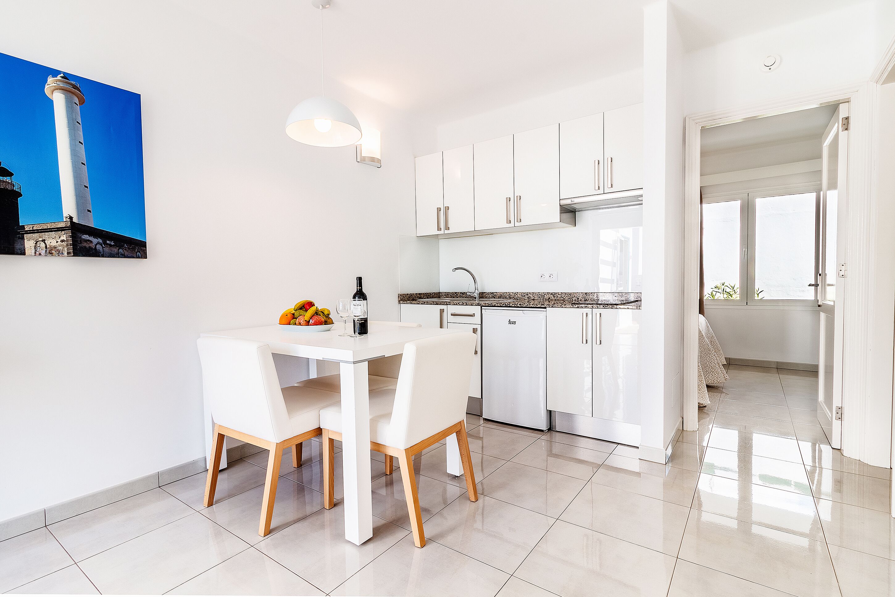 Een moderne keuken met witte kasten, een roestvrijstalen koelkast en een eethoek met een witte tafel en stoelen.