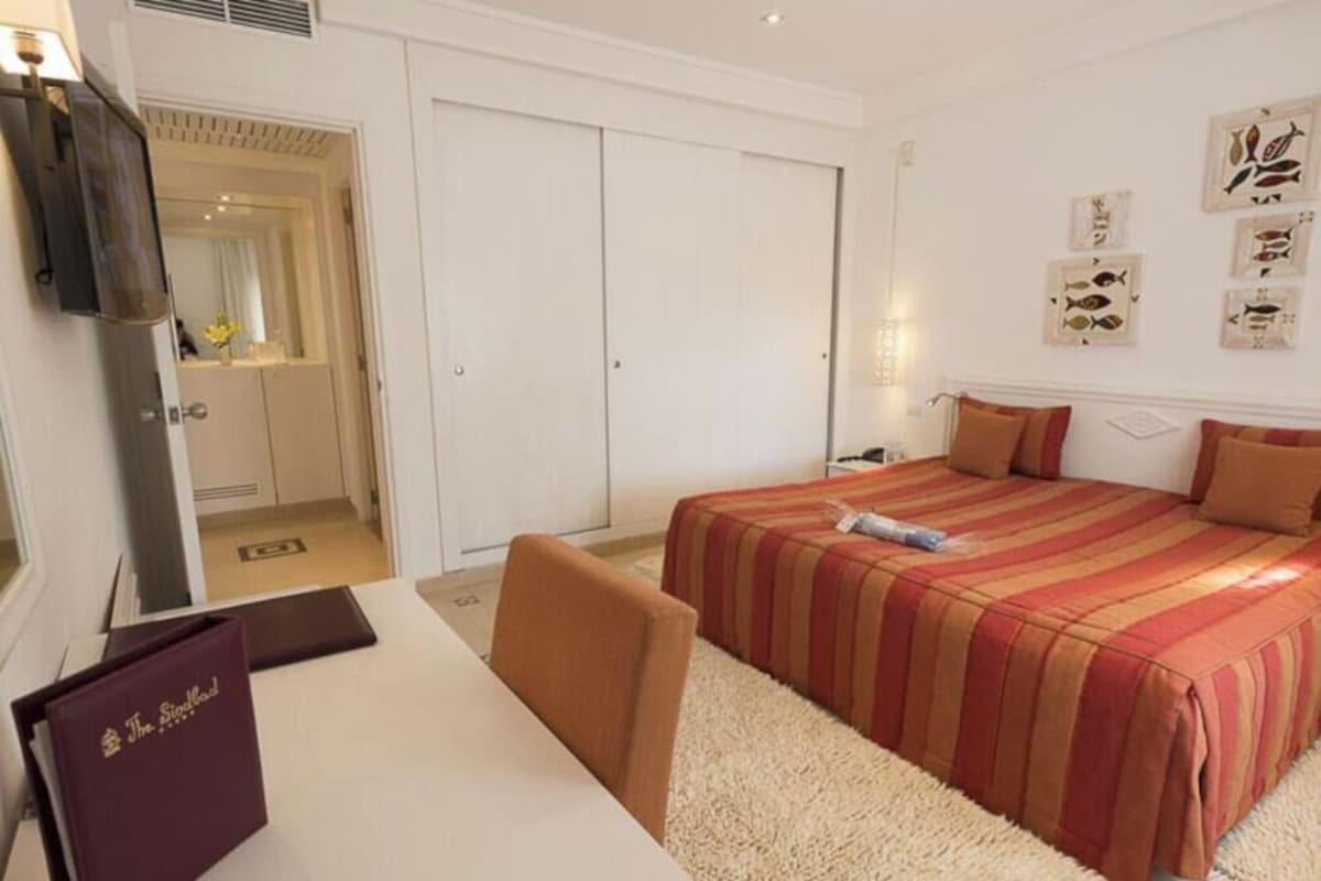 Una habitación de hotel con cama, escritorio, silla, armario y espejo.