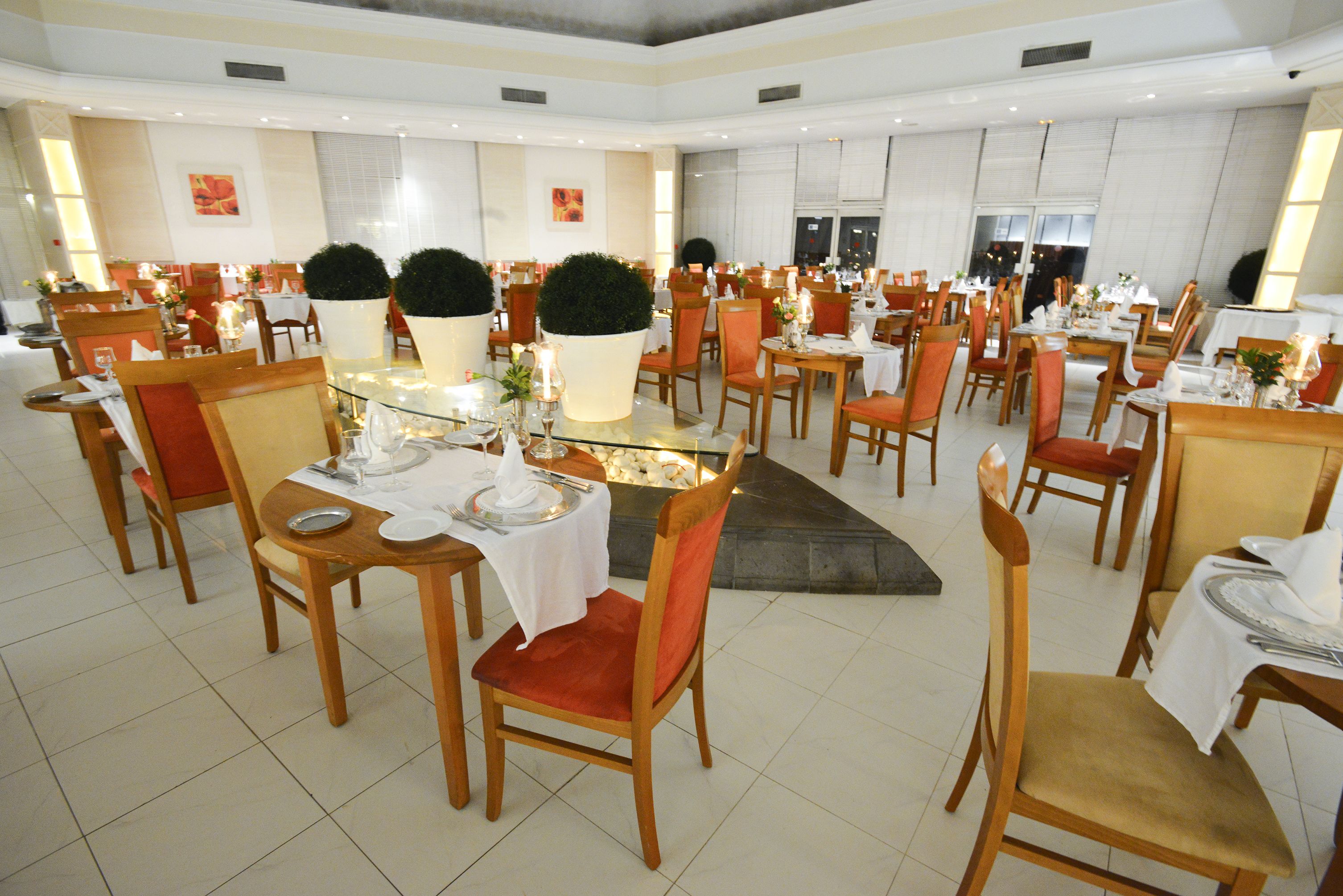 A spacious dining area with multiple tables and chairs, each set with white tablecloths and candles.