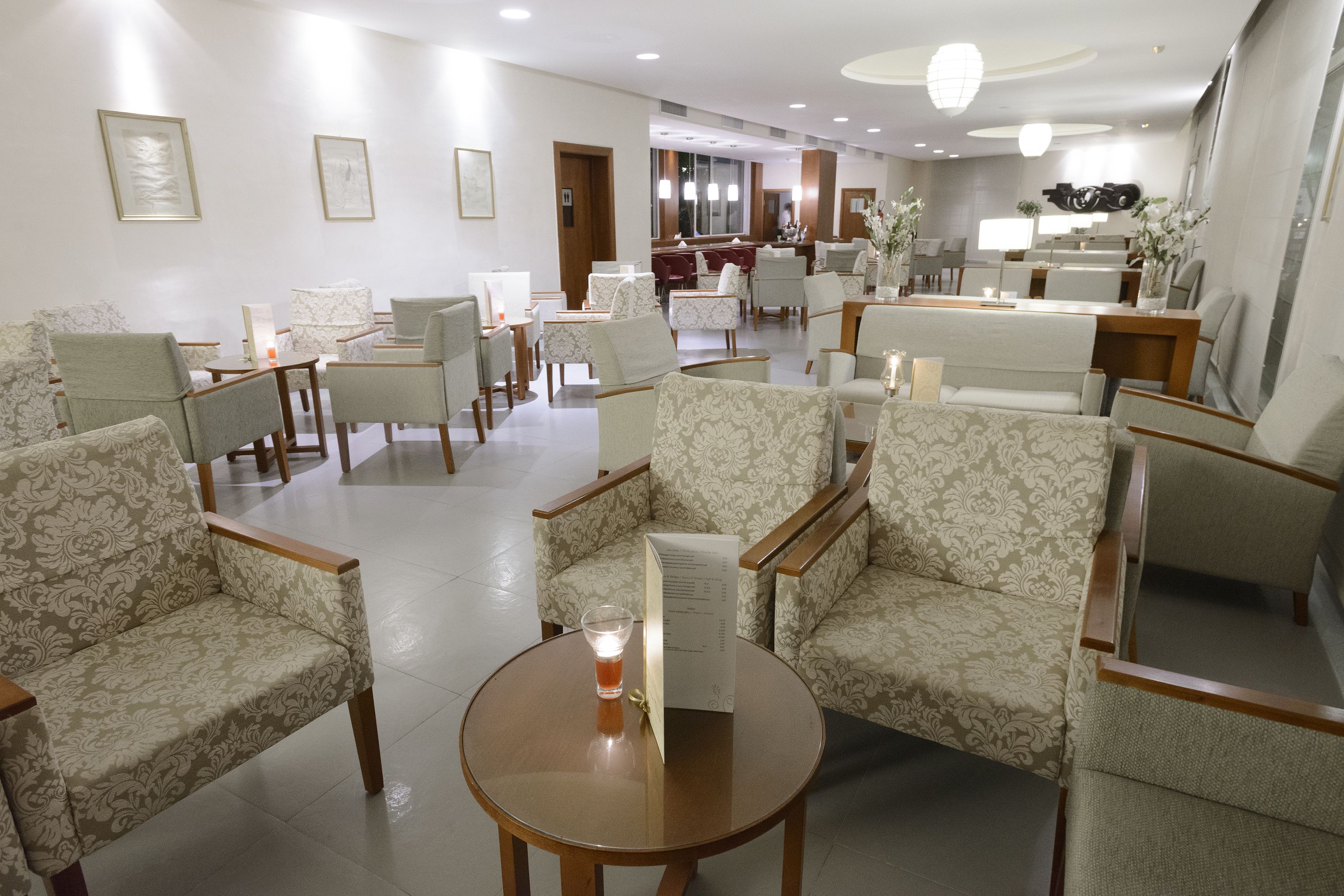 A hotel lobby with patterned armchairs, a round wooden table, and a reception desk.