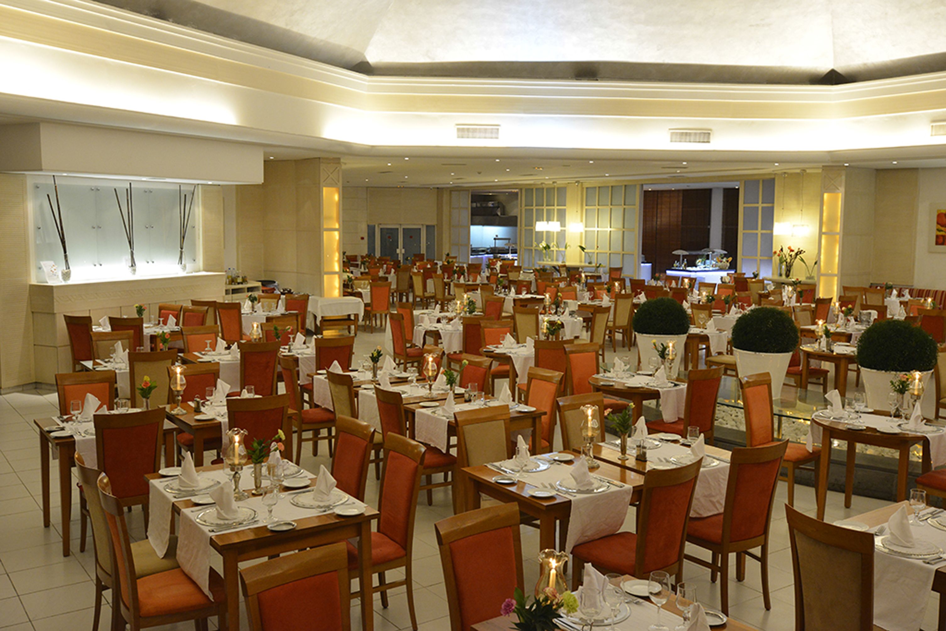 A spacious dining area with multiple tables and chairs, arranged in rows, with a kitchen visible in the background.