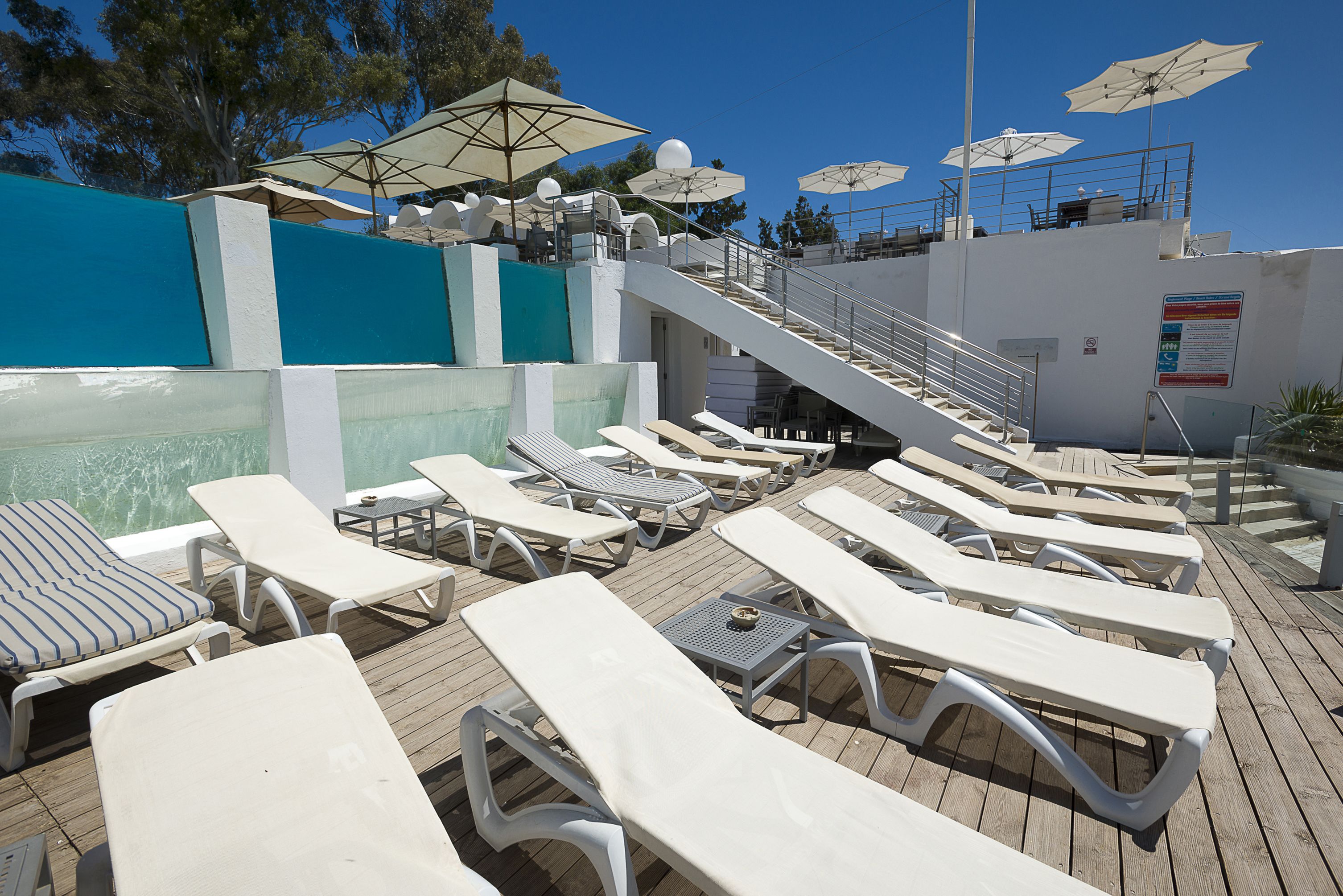 A poolside area with sun loungers, umbrellas, and a staircase leading to an upper deck.