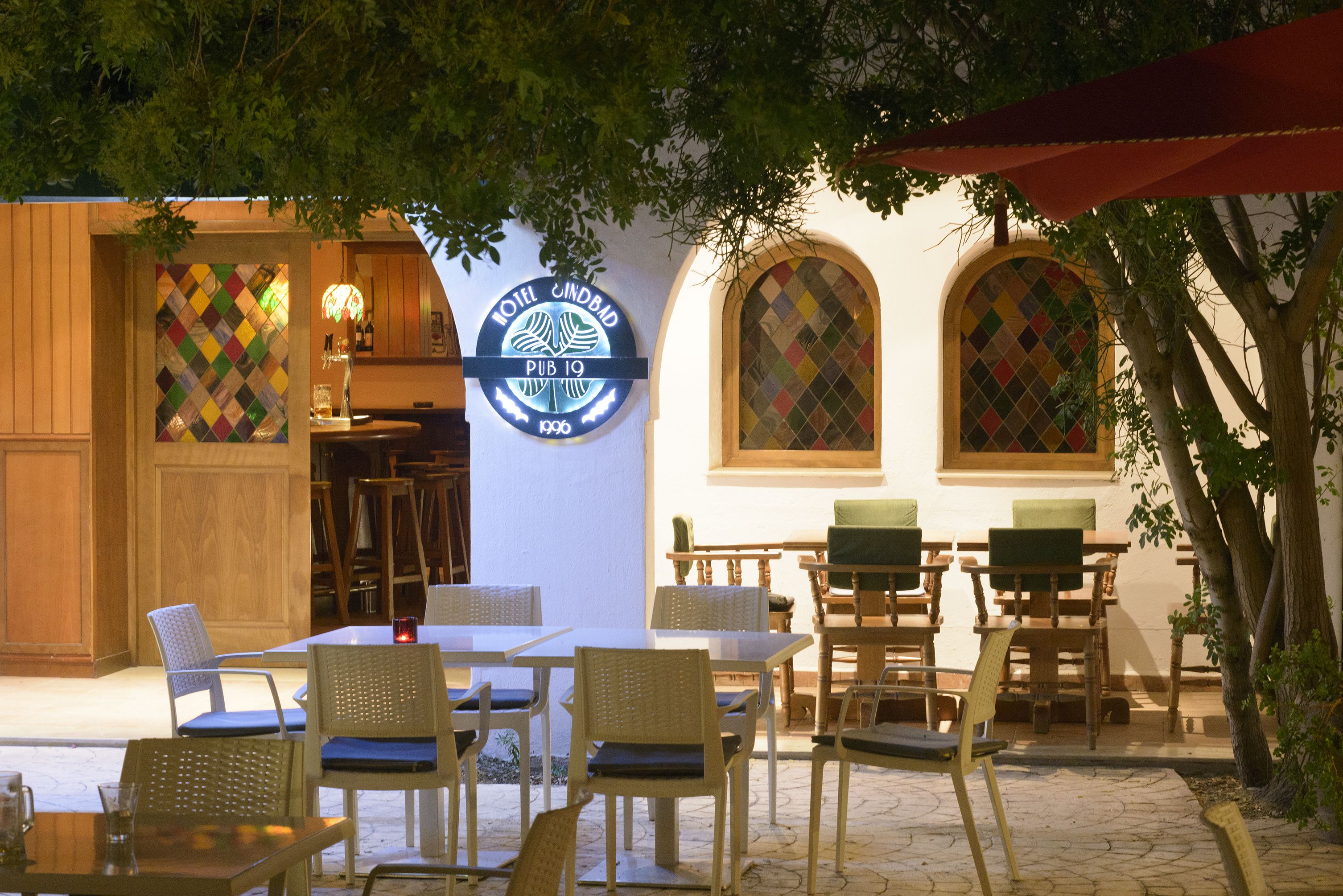 An outdoor seating area with tables and chairs, a sign for 'HOTEL CINDBAD PUB 10', and a patterned window.