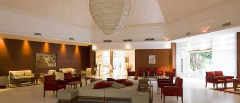 A spacious lobby with a large bed, red chairs, and a modern chandelier.