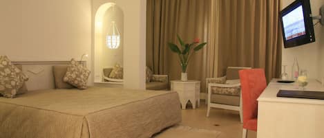 Habitación de hotel con una cama grande, un escritorio, una silla, un televisor y un florero con flores.