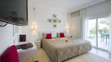 Een slaapkamer met een groot bed, een bureau met stoel, een televisie en een balkon met een stoel.