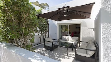 Un patio al aire libre con mobiliario de mimbre, una mesa de vidrio y un paraguas grande.