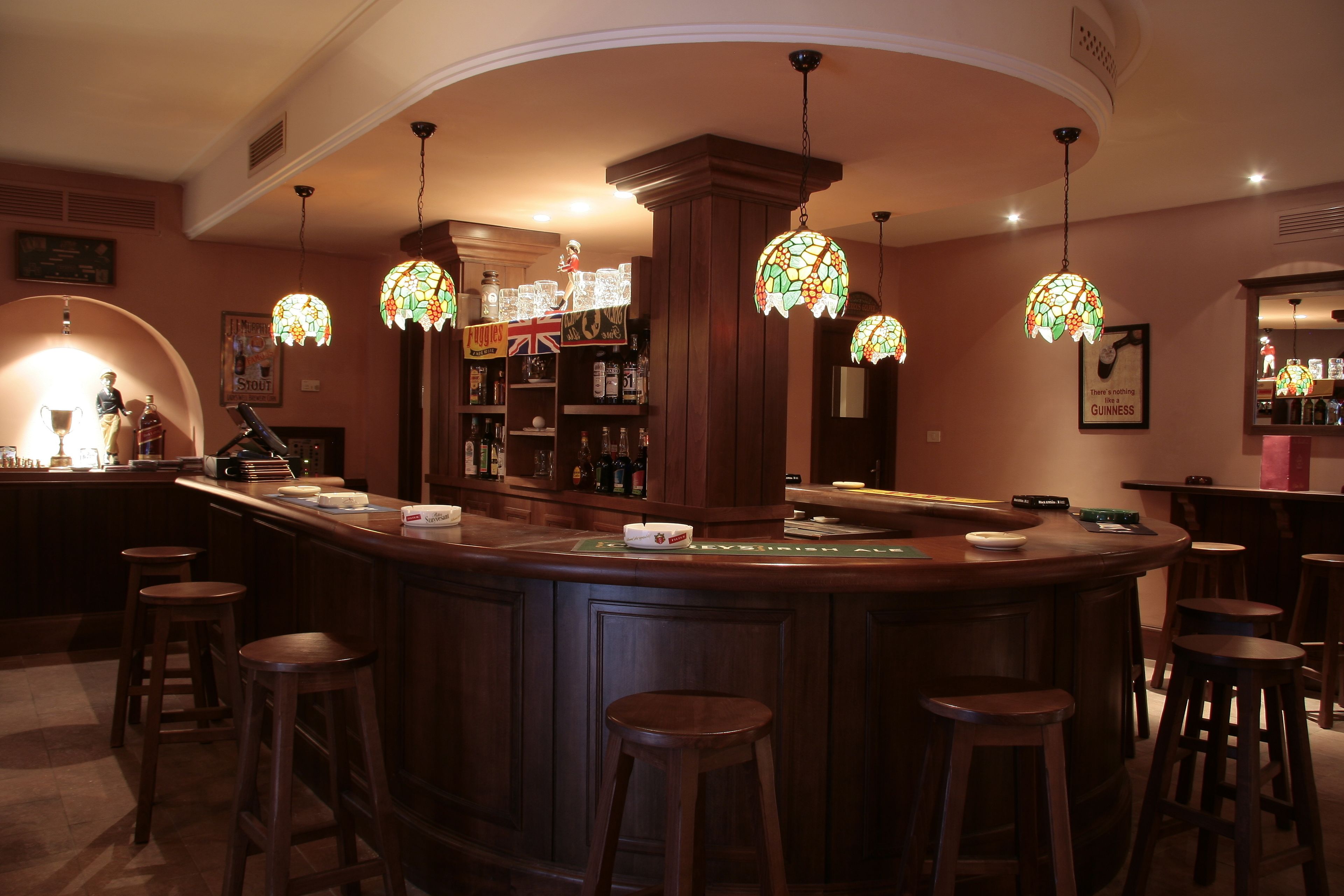 Un espace bar doté d’un comptoir en bois, de plusieurs tabourets et de luminaires suspendus en vitrail.
