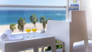 Una mesa blanca con dos vasos de zumo de naranja y una toalla enrollada en un balcón con vistas al mar.