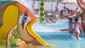A water slide shaped like a fish with a large blue eye, surrounded by a pool area with people and umbrellas.