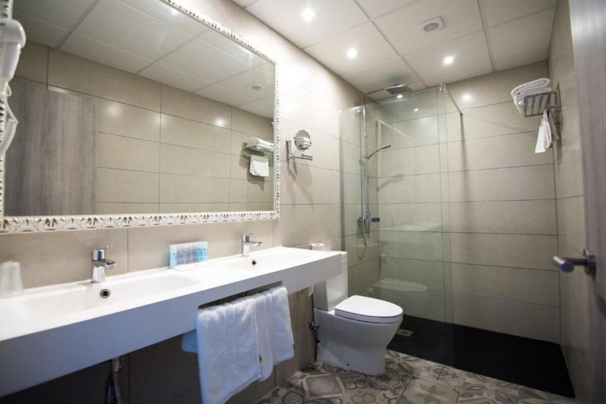 Een moderne badkamer met een grote spiegel, een witte wastafel, een toilet en een douchecabine met glazen wanden.