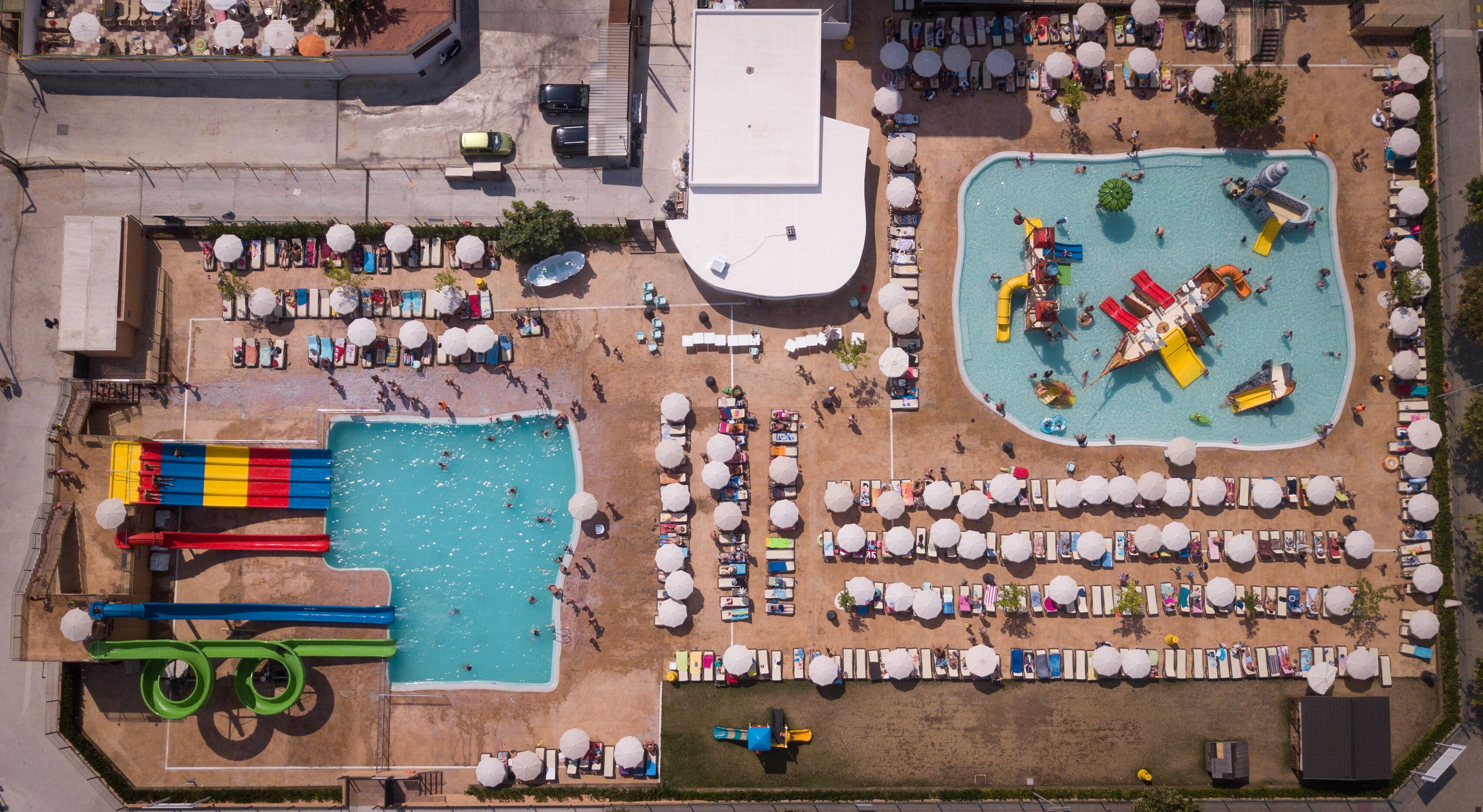 Een luchtbeeld van een resort met meerdere zwembaden, ligbedden en parasols.