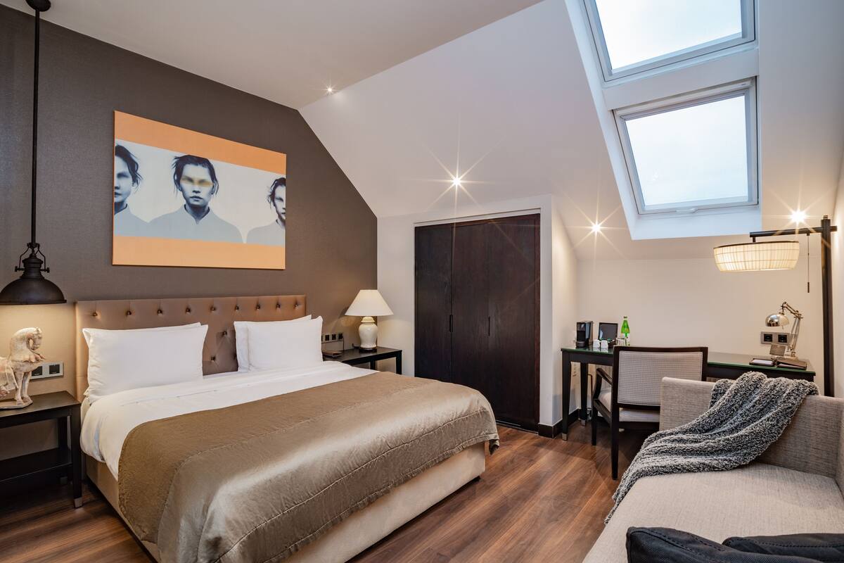 Ein modernes Hotelzimmer mit einem großen Bett, einem Schreibtisch, einem Sessel und einem Oberlicht.