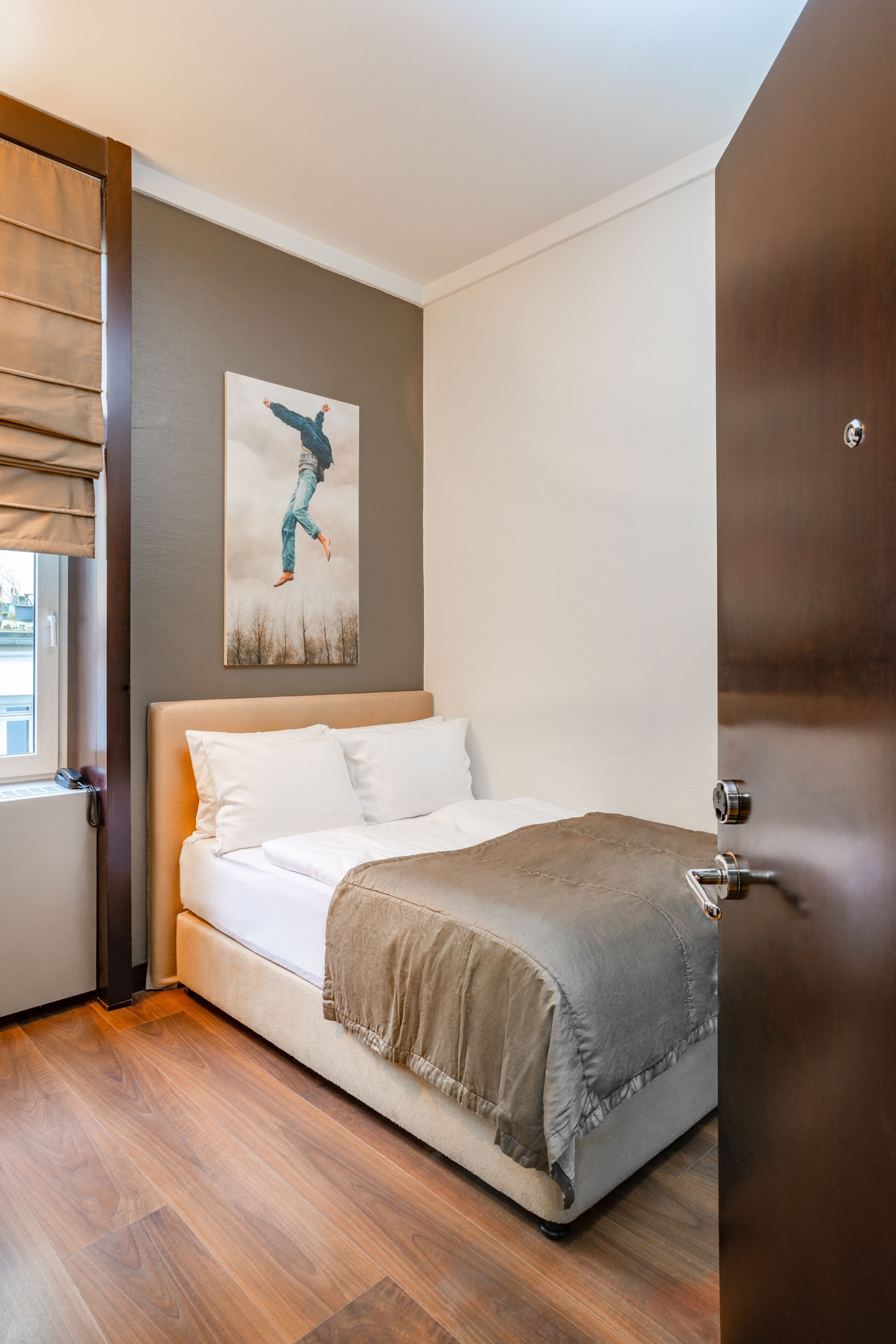 A neatly made bed with a beige headboard, a gray blanket, and a white pillow.