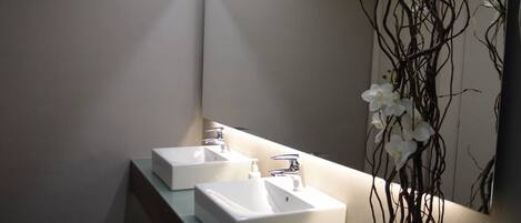 A modern bathroom with two white sinks, a mirror, and a decorative orchid plant.