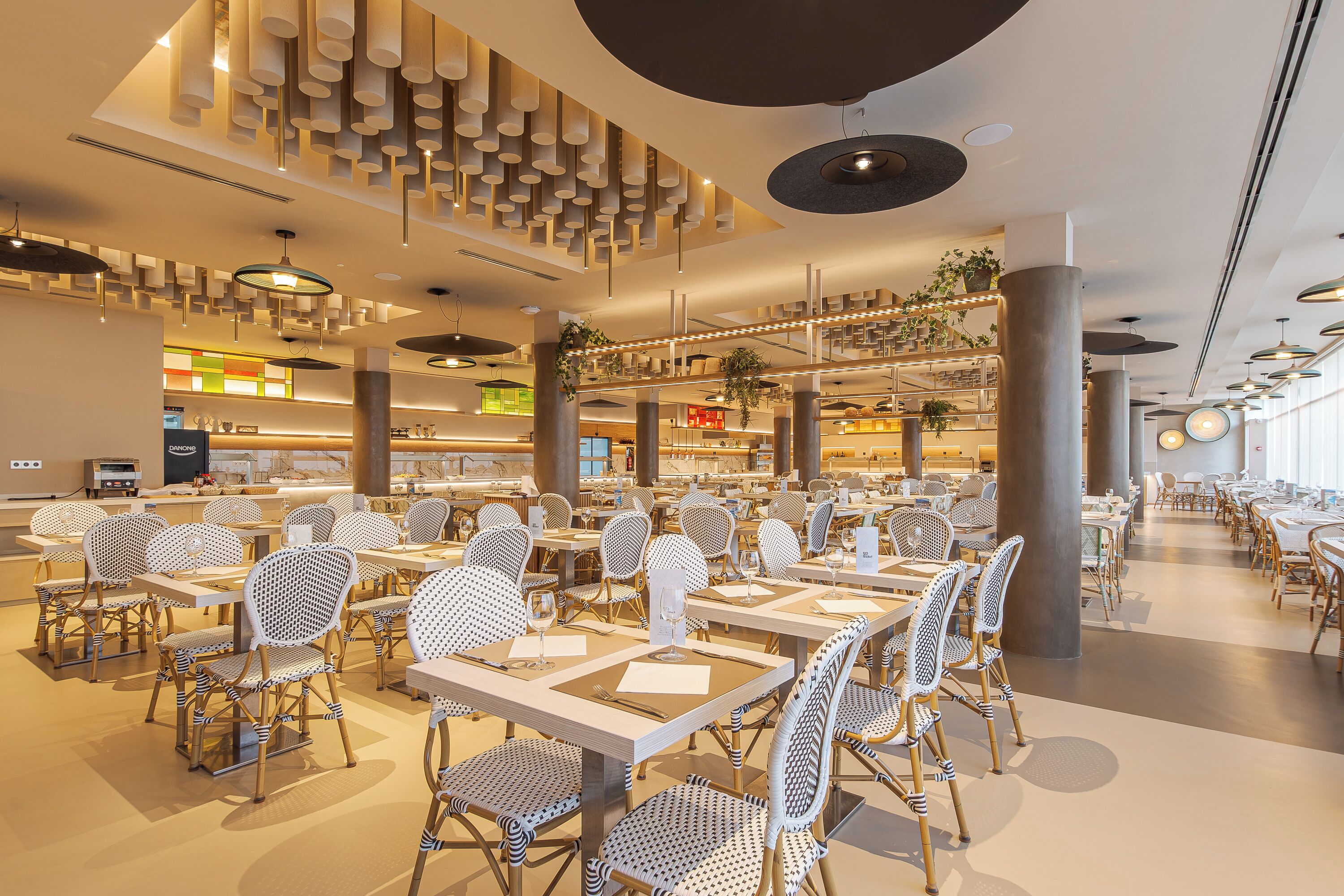 A spacious restaurant with high ceilings, modern lighting fixtures, and a variety of seating arrangements including tables and chairs.